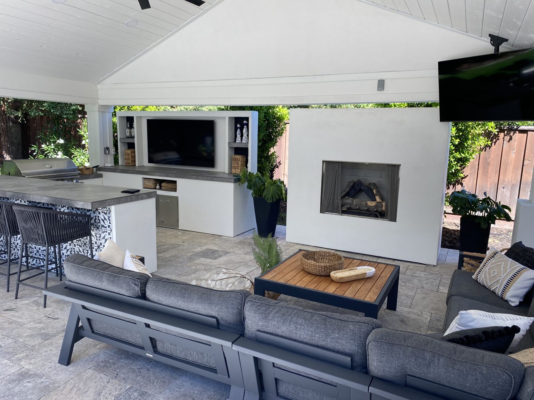 Covered outdoor living room with TV wall, fireplace, sectional sofa and grill bar