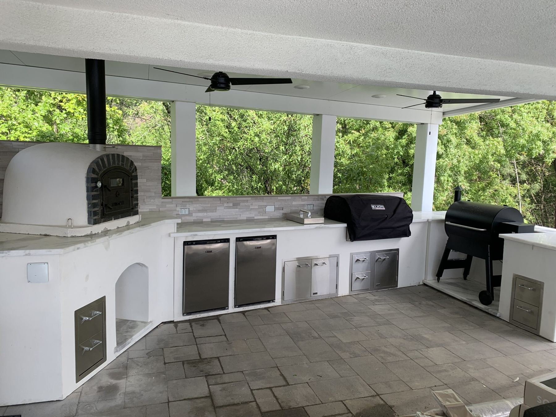 Covered patio kitchen with a domed pizza oven, stainless doors and drawers and a smoker